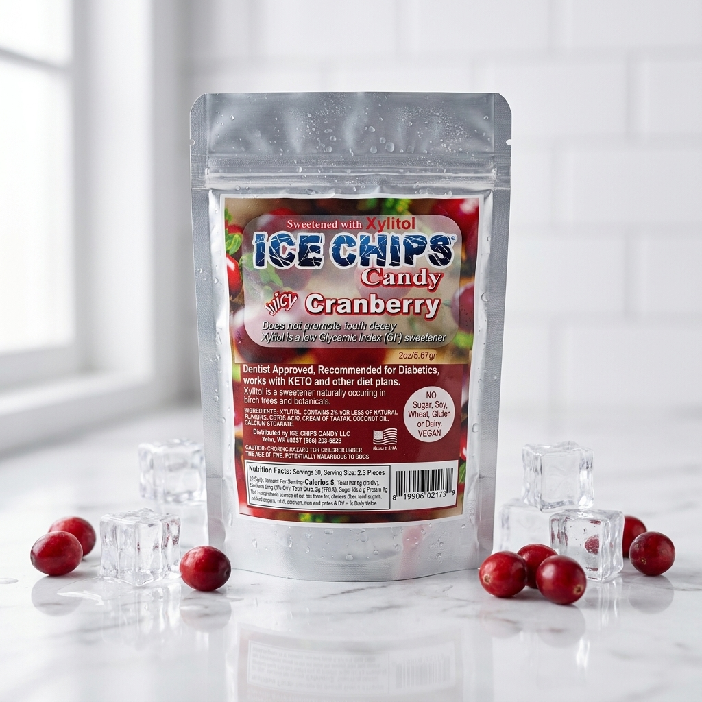 A stand-up pouch of Ice Chips Candy Cranberry flavor, surrounded by scattered cranberries and clear ice cubes on a glossy white surface with a white subway tile wall in the background.