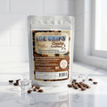 A stand-up pouch of Sweetener Free Xylitol Ice Chips Candy Coffee, surrounded by scattered coffee beans and clear ice cubes on a reflective white surface.