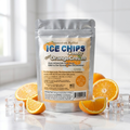 A stand-up pouch of Xylitol Ice Chips Candy in Orange Cream flavor, styled on a white marble surface with sliced oranges and ice cubes. The background is a bright, softly blurred kitchen setting.