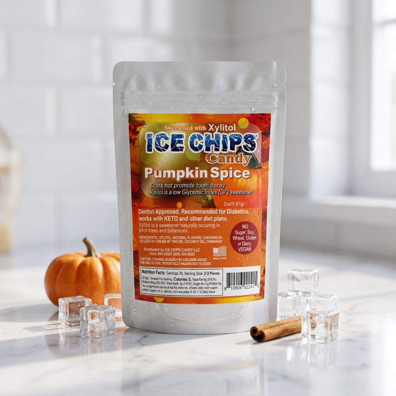 A stand-up pouch of Ice Chips Candy Pumpkin Spice candy sits on a marble surface with a small pumpkin, ice cubes, and a cinnamon stick around it. The package is white with a large orange and yellow label, and the background is a bright, softly blurred kitchen-like setting.