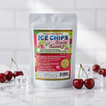A stand-up pouch of Sour Cherry Ice Chips Candy, displayed on a marble surface with fresh cherries and ice cubes around it against a white tiled background.
