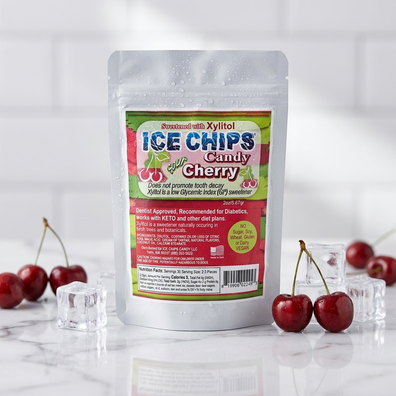 A stand-up pouch of Sour Cherry Ice Chips Candy, displayed on a marble surface with fresh cherries and ice cubes around it against a white tiled background.