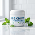 A white plastic jar of ICE CHIPS Tooth Powder in the Minty Fresh flavor, styled on a white marble surface with mint leaves and clear ice cubes against a white subway tile background.